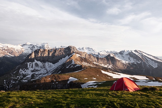 Red ten pitched in a field at the botom of snow capped mountains